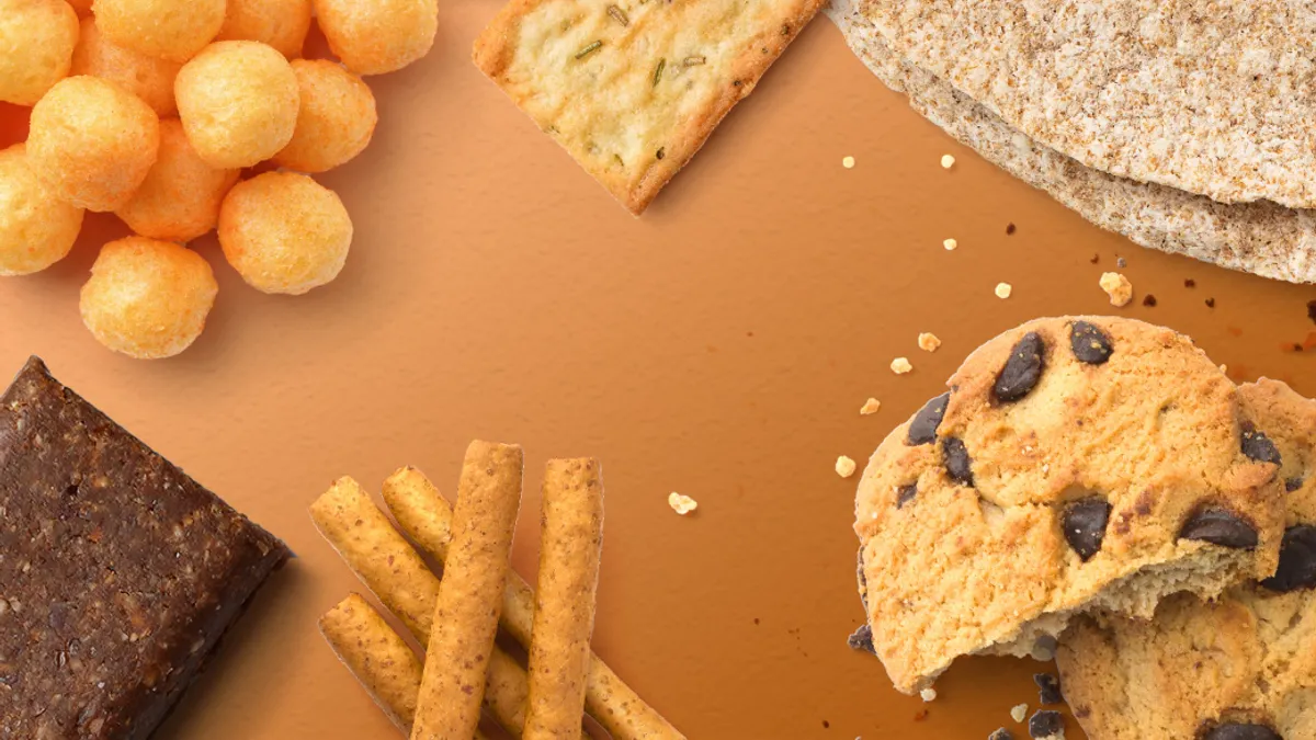 An assortment of cheese puffs, chocloate chip cookies, and other plant based baked goods against a brown background.