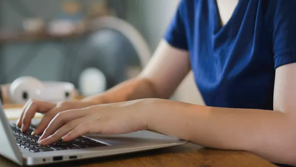 A high school student's hands are seen typing at a keyboard.