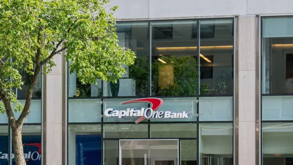 A commercial building with large windows; the sign “Capital One Bank” appears in white letters with a red swoosh over a glass entrance.