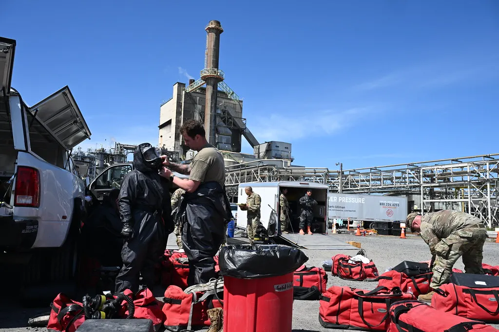 People unpack gear and put on protective suits at the exterior of an industrial facility.
