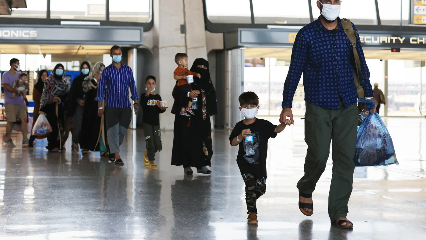 People of all ages arrive at an airport wearing masks and carrying bags and water bottles.