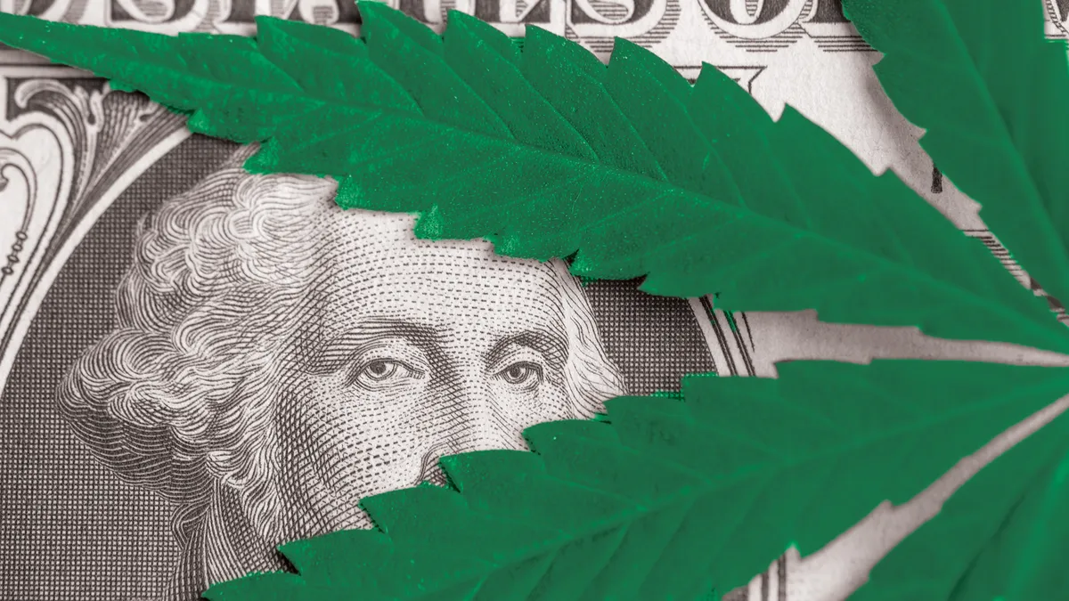 A cannabis leaf placed on a one dollar bill partially shields President George Washington's portrait.