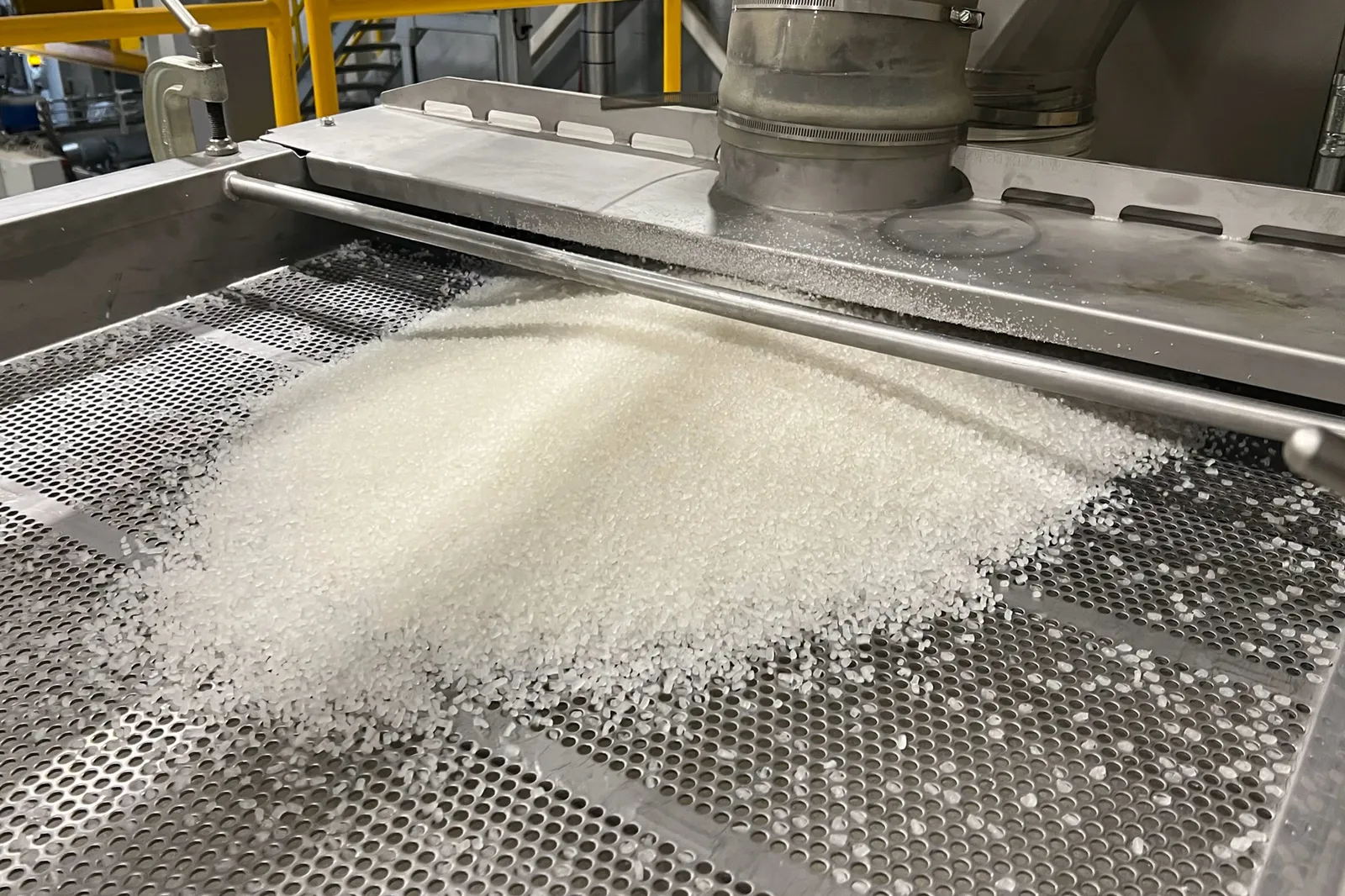 A pile of clear polypropylene resin pellets sits on a screen in a factory.