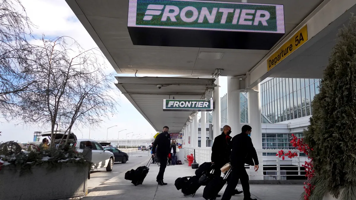 People with luggage enter an airport below a Frontier sign.