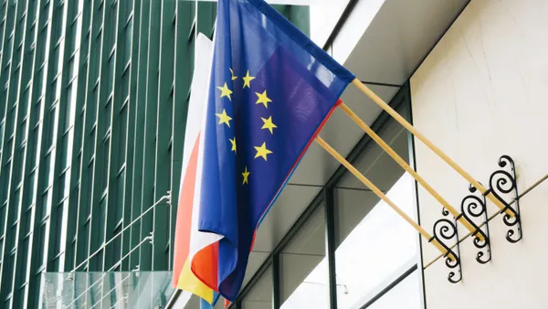 The European Union flag hags at the entrance of a modern glass office building.