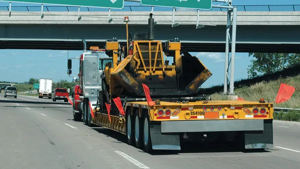 A digger on a flatbed truck on the highway.