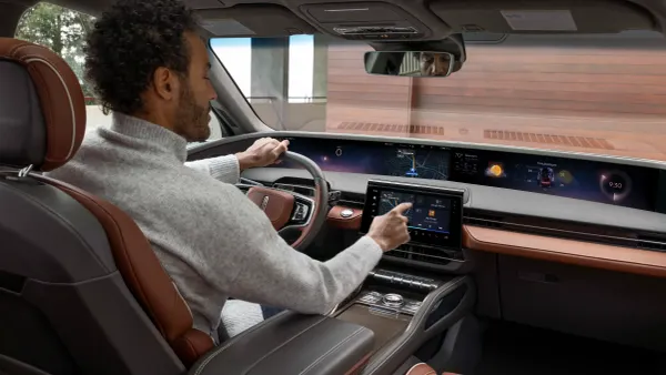 A driver wearing a grey turtleneck sweater interacts with the infotainment screen in a luxury Lincoln vehicle.