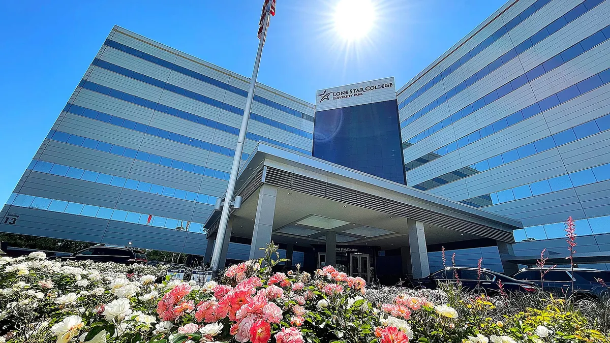 Modern office building behind "Lone Star College" sign, with flower in foreground and flowers in background.