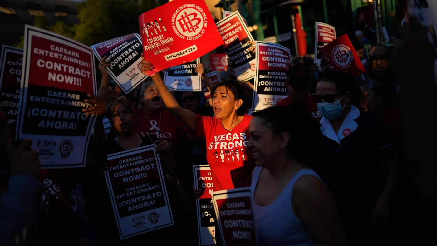 One person in a crowd is illuminated. The person wears a shirt reading "VEGAS STRONG" and holds a sign for the Culinary Workers Union.