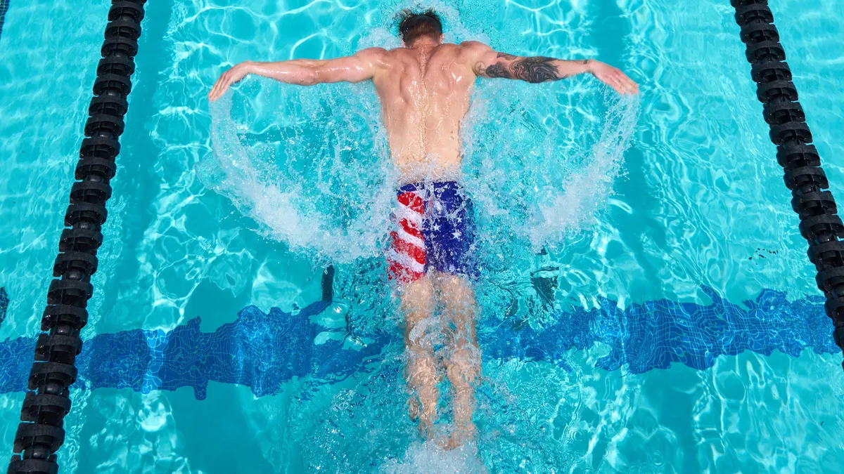 Swimmer Steele Johnson dives into a poll wearing American flag-themed swim trunks