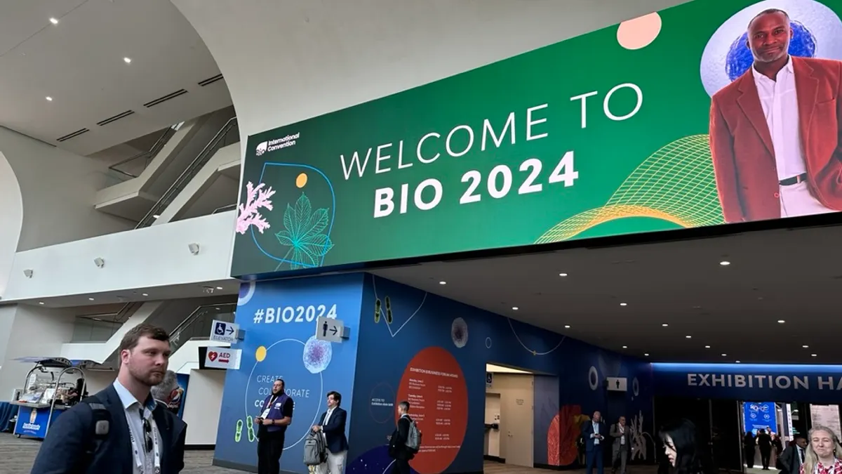 People walk past a sign reading BIO 2024 in a conference center.