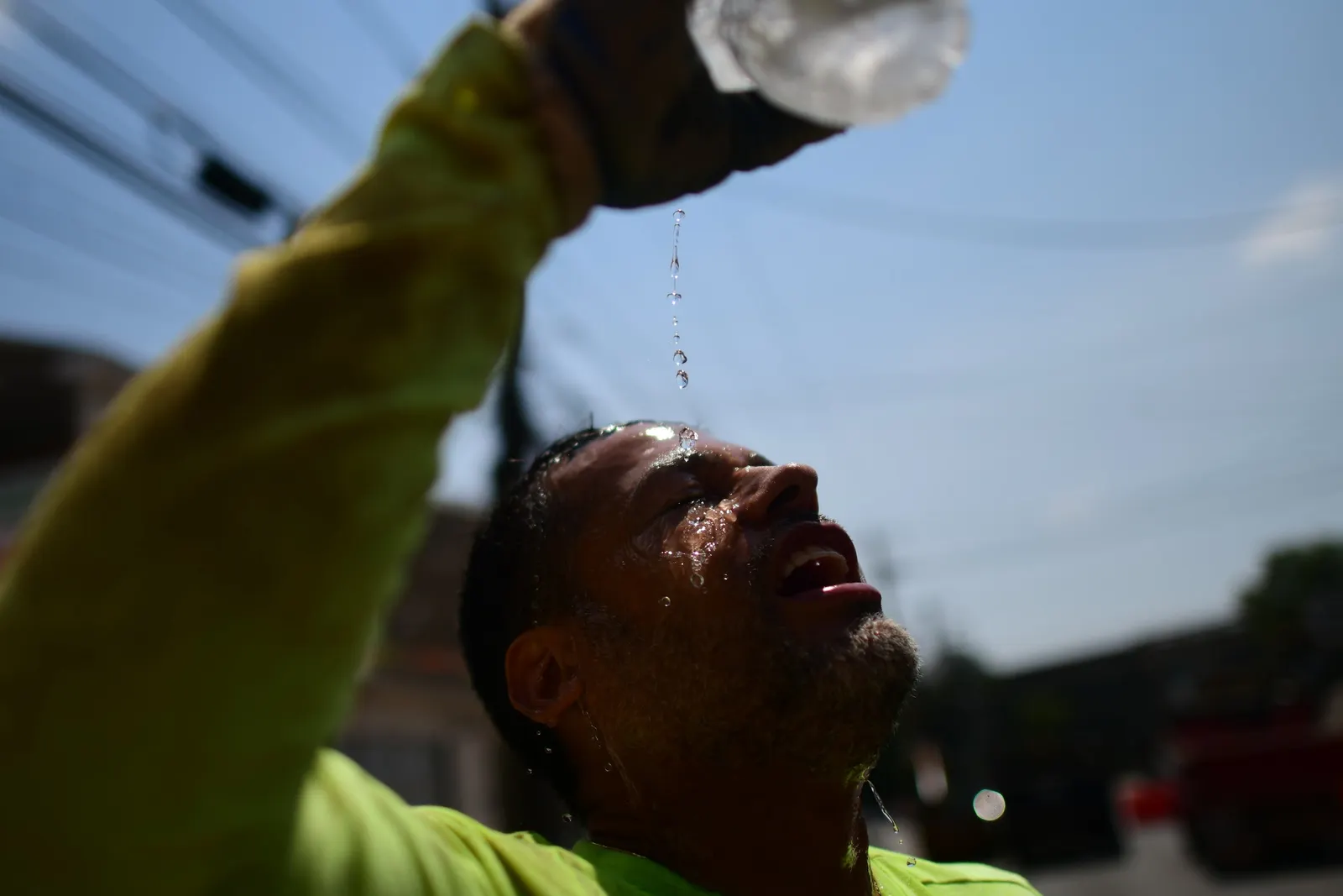 A person pours water from a plastic bottle on their face.
