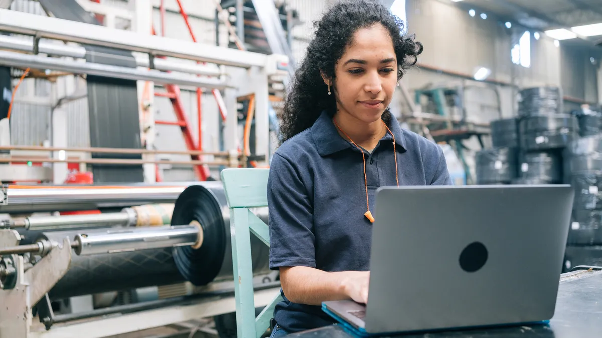 A person types on a laptop in front of heavy equipment.