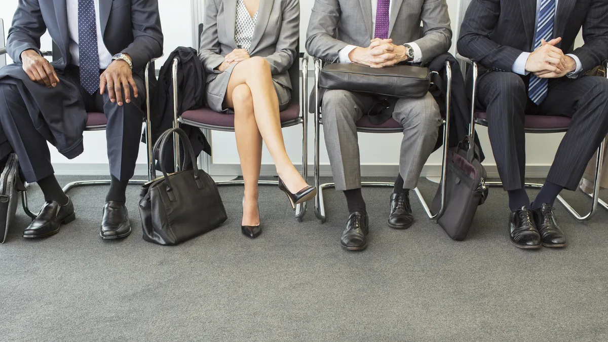 A row of individuals in suits wait in a room for a job interview