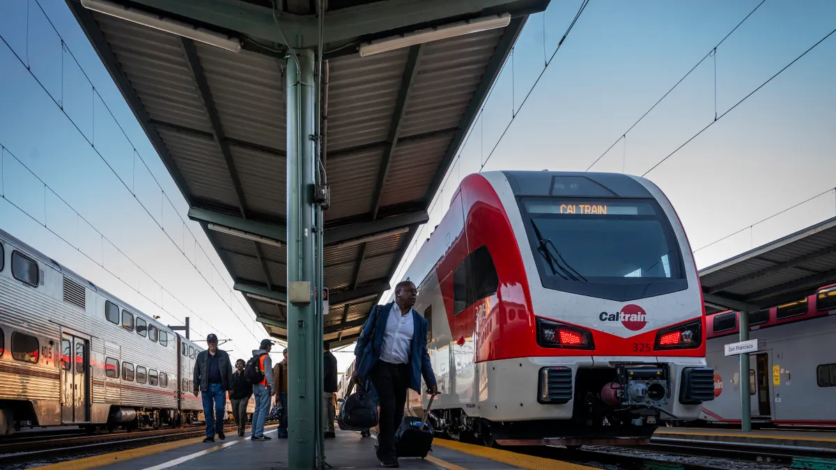Low angle view of people on a train platform under a canopy with a red and white self-propelled passenger train alongside marked Caltrain.