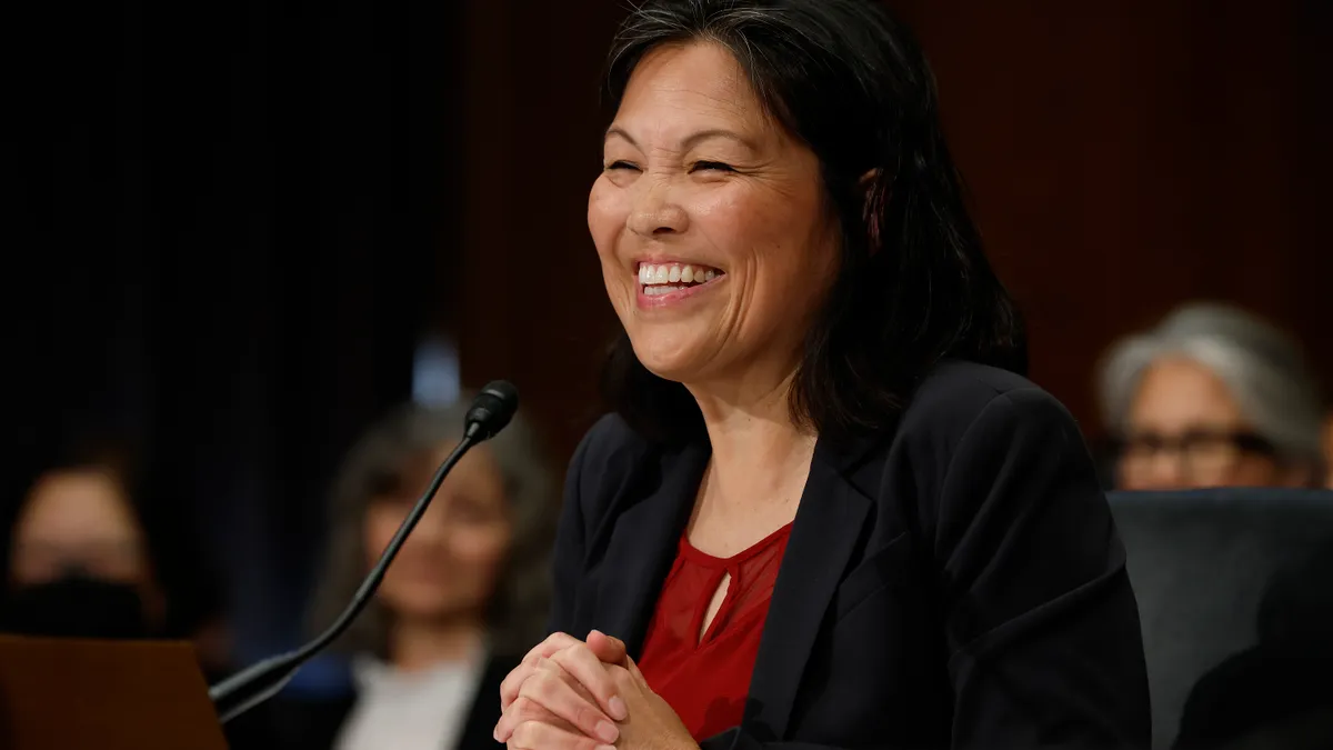 A woman smiles, as she sits in front of a microphone.