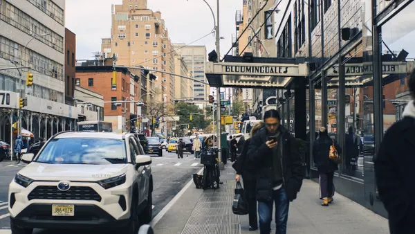 People walking down the street and cars driving in a city.