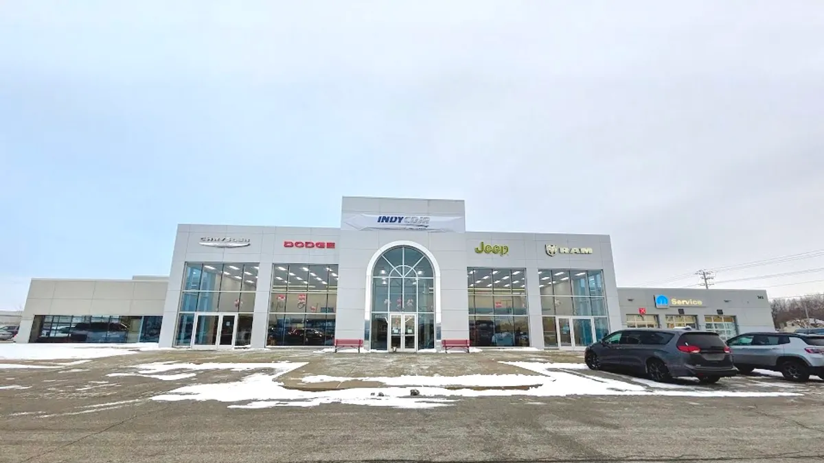 A large white building with the sign "Indy CDJR" has vehicles parked in front and Chevy, Dodge, Jeep and Ram logos on the wings.