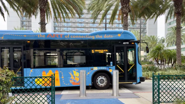 A blue transit bus with crayon-like art decor with a large hotel behind it.