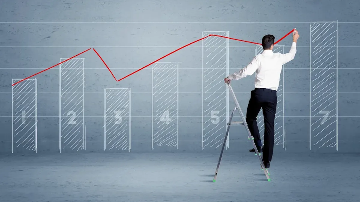 A man in a suit standing on a ladder and drawing a chart on blue wall background
