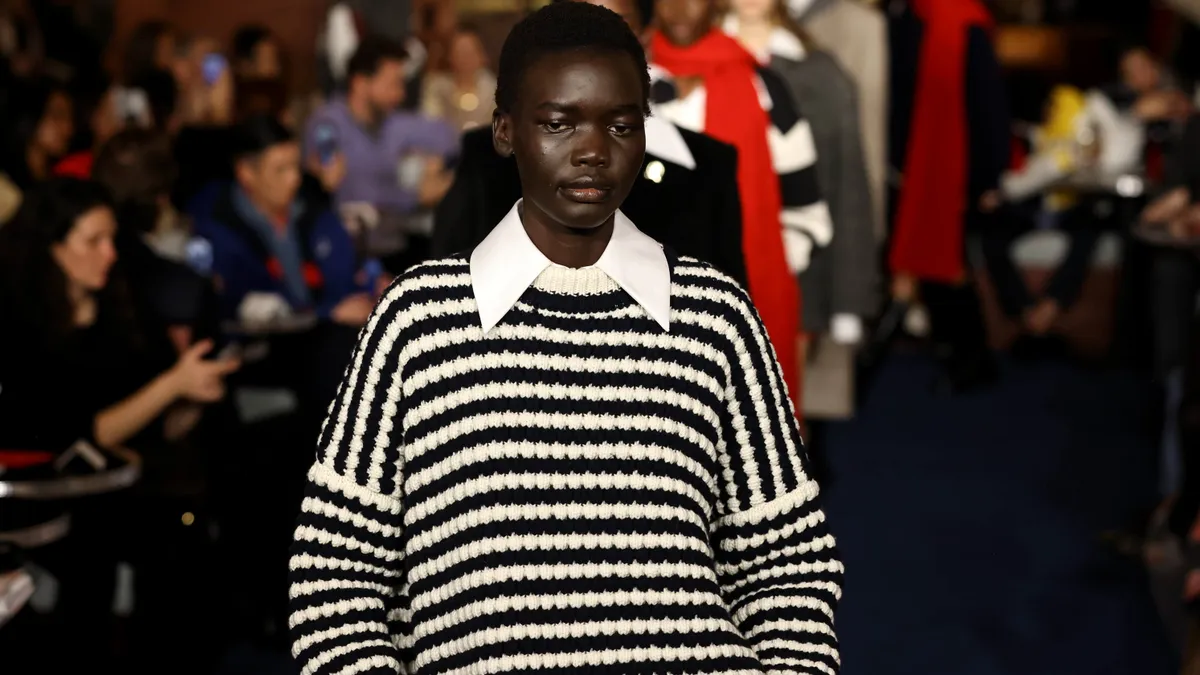 A model in a black and white striped oversized sweater stares at the camera on the runway during a Tommy Hilfiger fashion.