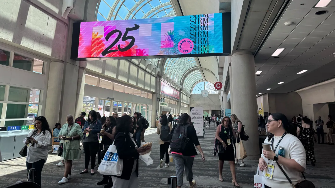 SHRM25 attendees walk under signage for the conference.