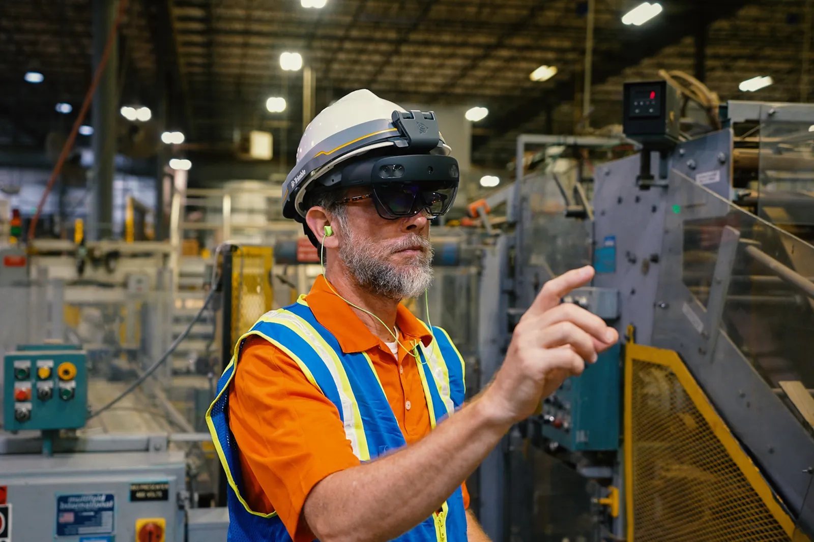 A person wearing a hardhat and an augmented reality headset stands in an industrial facility.