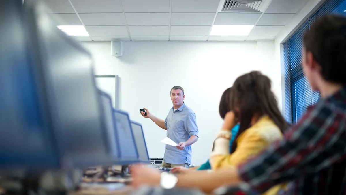 Students sit at computer terminals in a classroom.