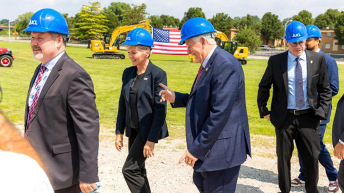 People in business clothes and blue hardhats have a cheerful conversation on a bright, sunny day.