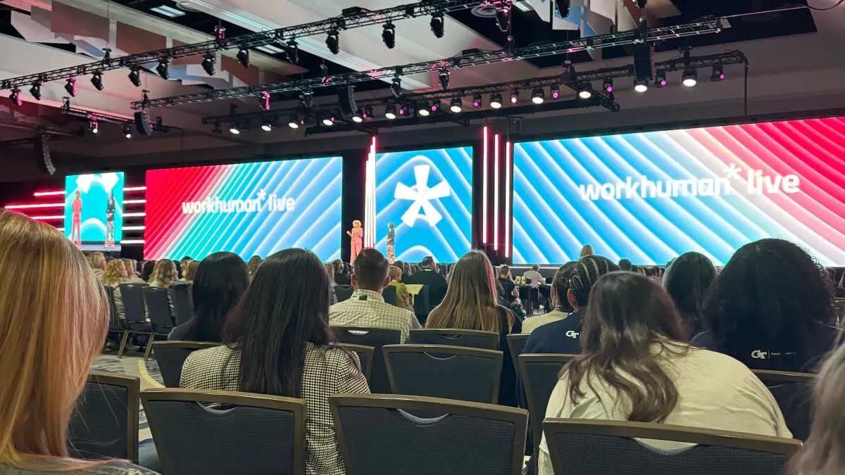 A view of a stage with "Workhuman" on the screen and the backs of people's heads in the audience.