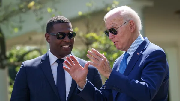 Two people wearing sunglasses talk to each other in front of a blurred background