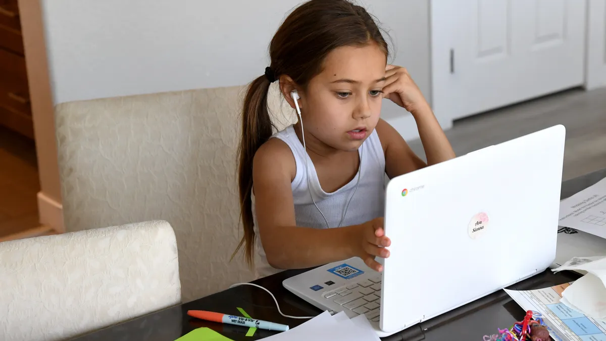 A female 3rd-grade student sits at a home table while participating in online learning during the COVID-19 pandemic.