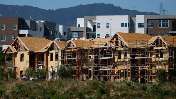 A row of unfinished houses at various stages of construction under a blue sky with mountains in the background.