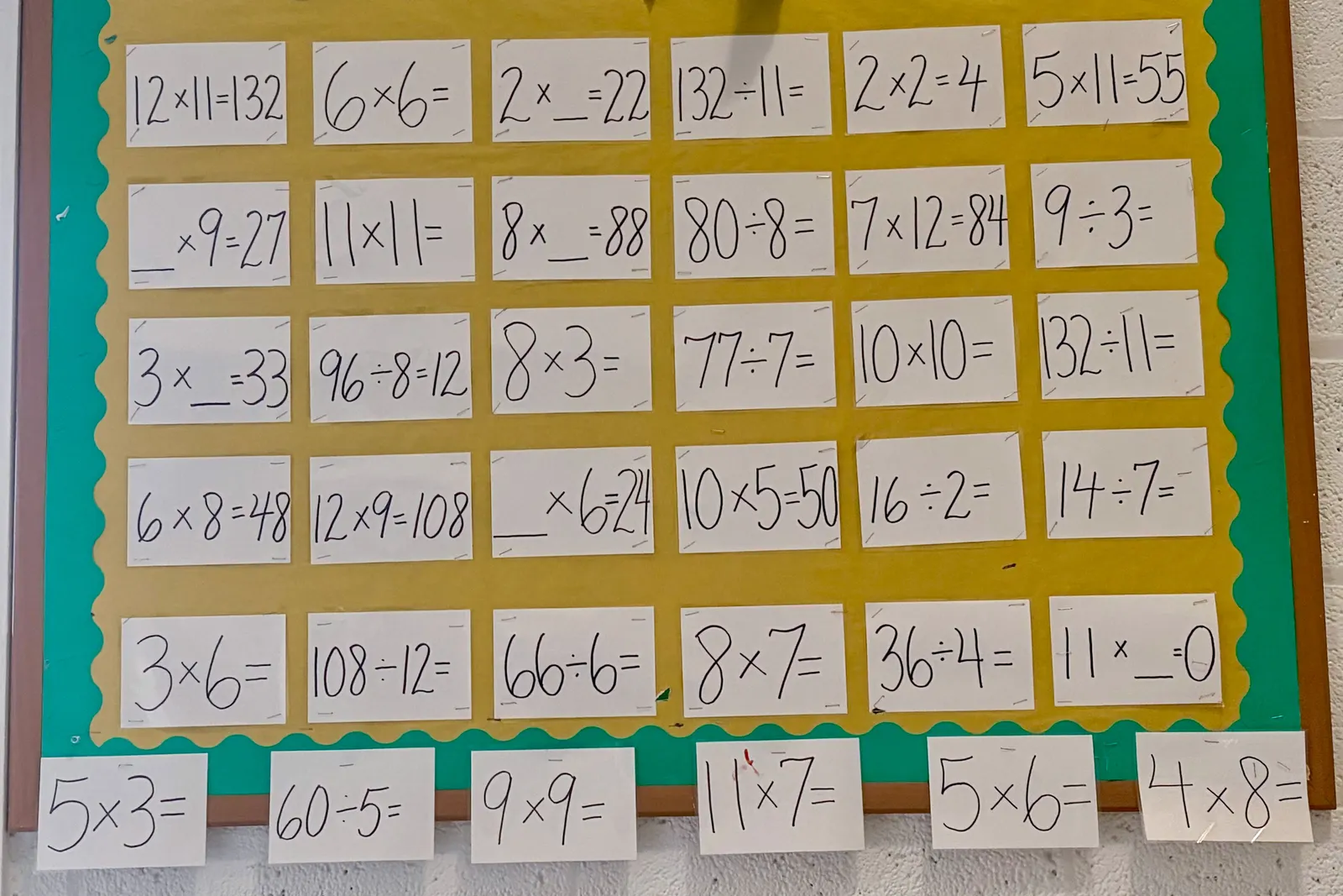A bulletin board in a school hallways shows many math multiplication and division problems with most answers left unfinished