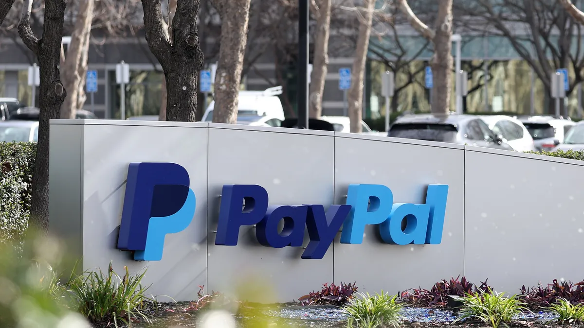 PayPal sign outside in front of parking lot with cars in background.