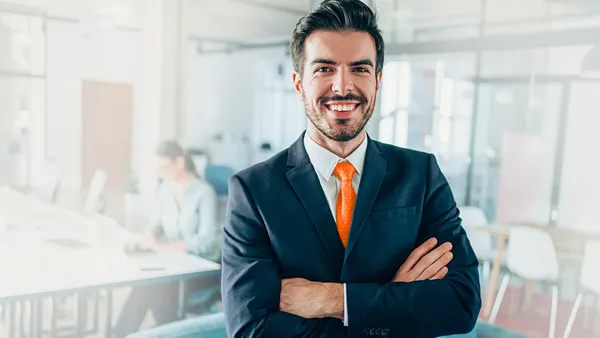 Smiling businessperson standing with arms crossed in modern office and looking at camera.