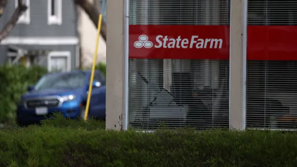 A State Farm sign hangs in the window of a building, and on the left, a blue car drives by in the street in the distance.