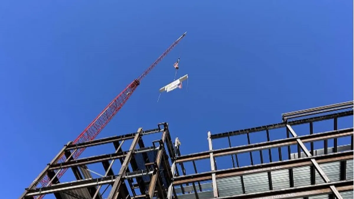 A construction crane puts a final steel member in place atop a building frame against a clear blue sky.