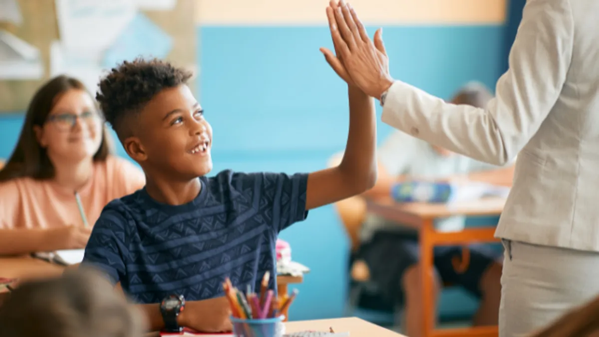 Happy African American schoolboy giving high-five to his teacher during class in the classroom.