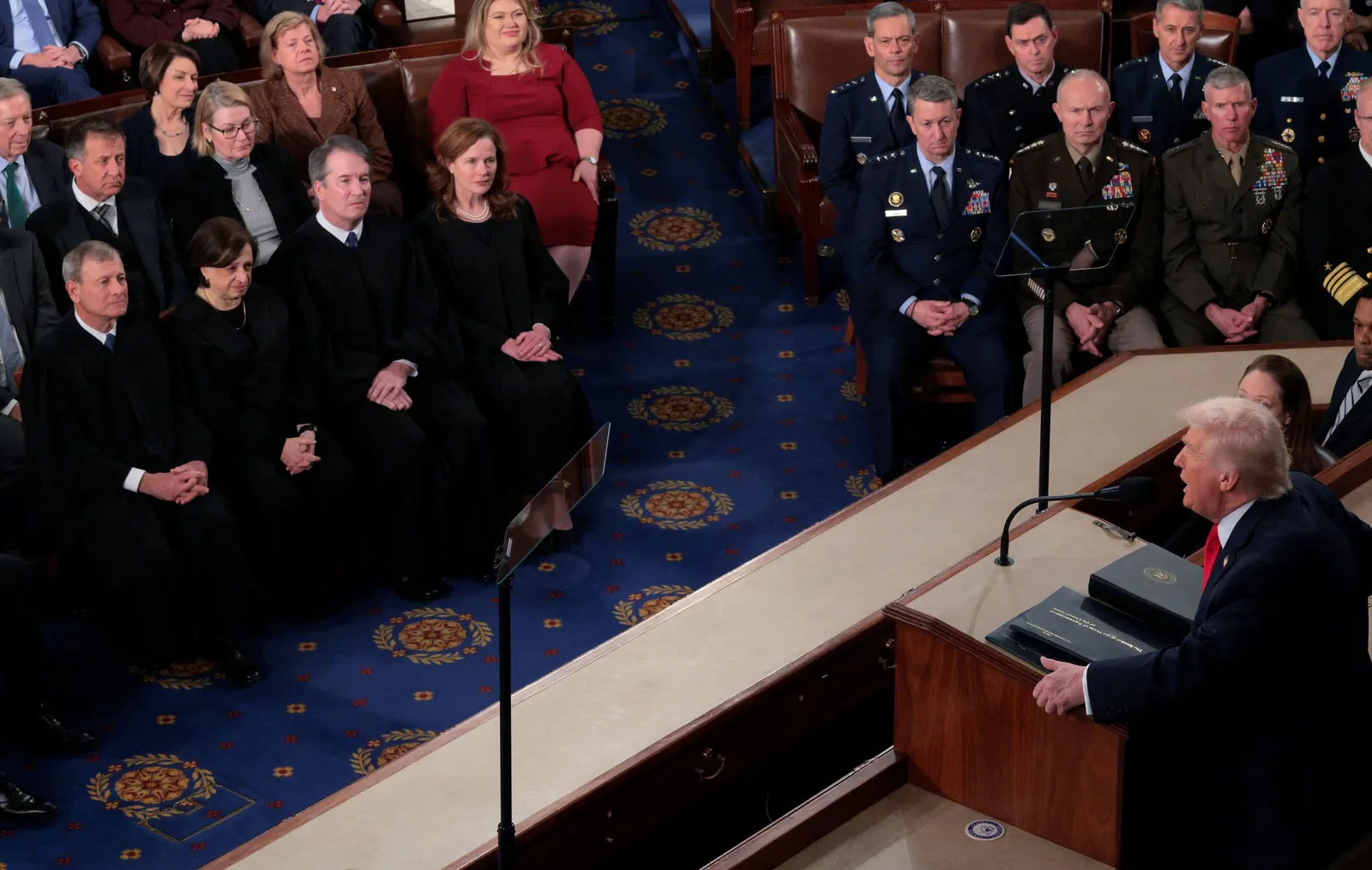 A man delivering a speech from a lectern to people in military uniforms and judges' robes