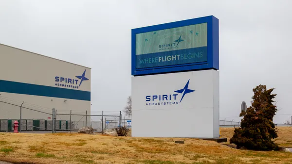 A beight and blue Spirit AeroSystems sign in with a beige and blue facility in the background.