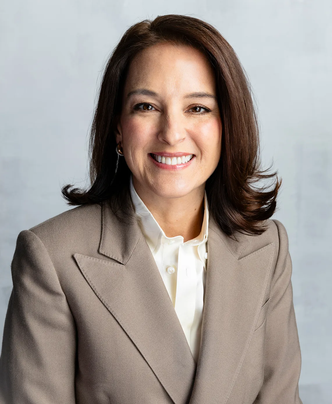 A person wears a beige jacket in a corporate headshot.