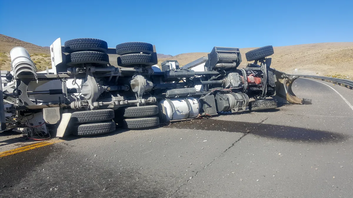 A truck overturned on its side in the middle of the roadway.