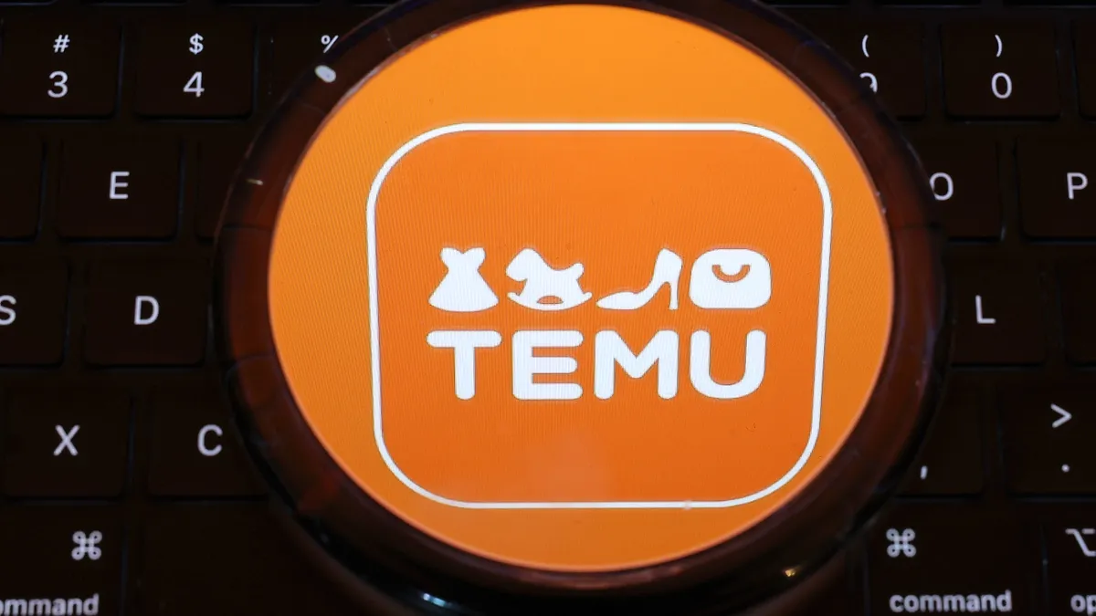 A Temu logo, which features various cartoon product symbols in orange, is seen over a laptop keyboard.