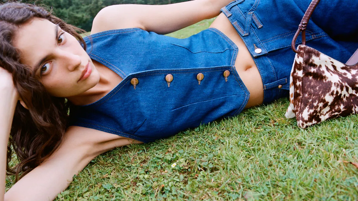 A person reclines on the grass wearing a denim vest and denim jeans.