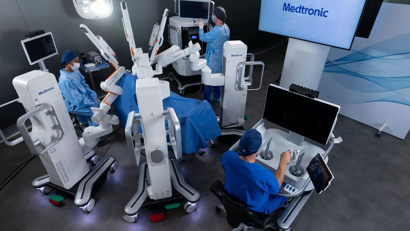 Three clinicians work with a robotic surgery system as a patient lies on the operating table.