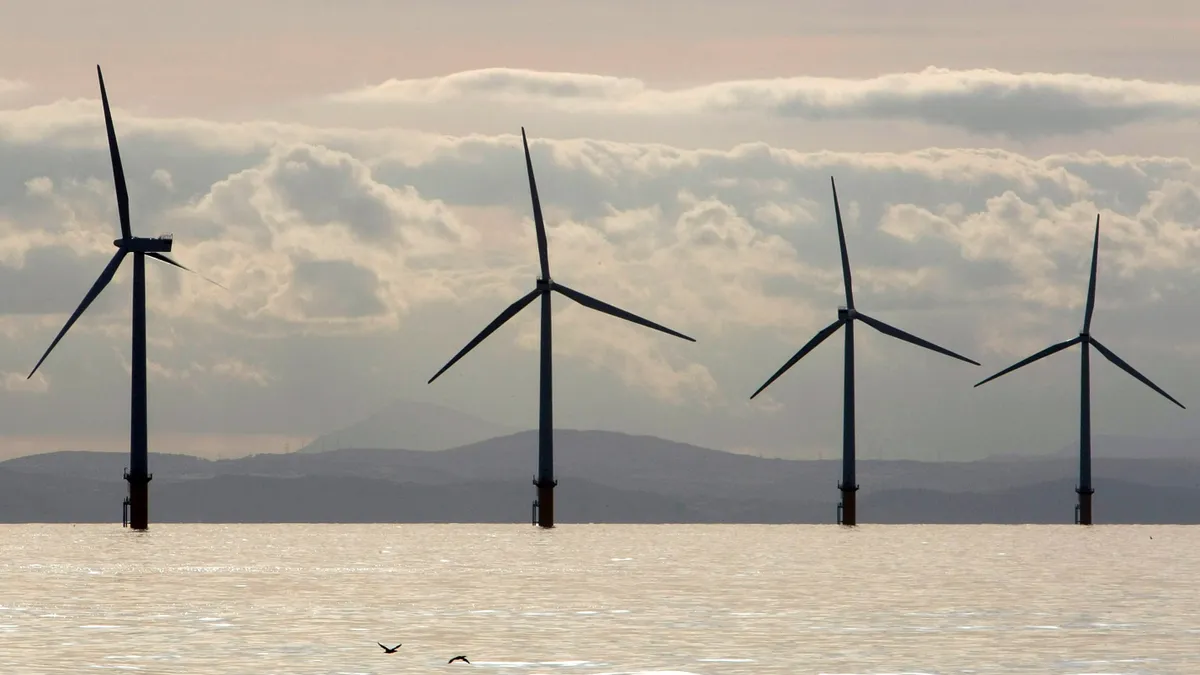 Offshore wind turbines sit in the ocean in front of a cloudy sky in England.