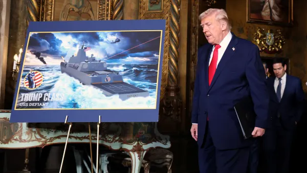 A person in a three-piece suit and red tie walking past an easel with a ship on an ocean rendering.
