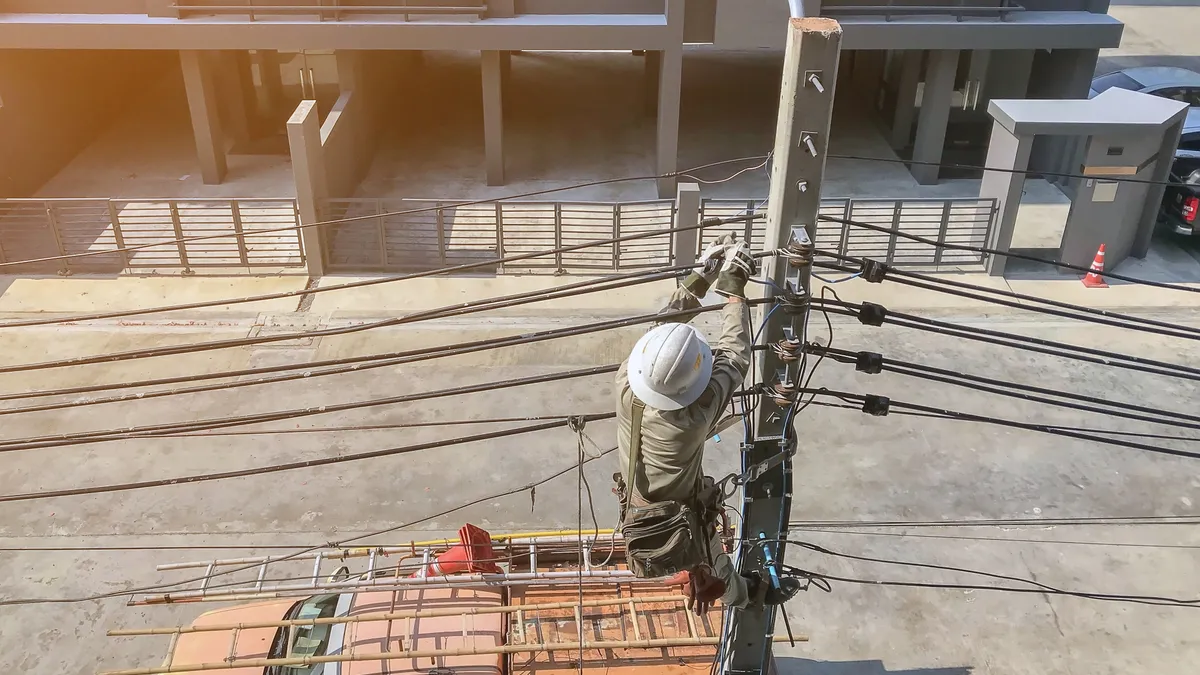 A utility worker works on power lines outside of a building.