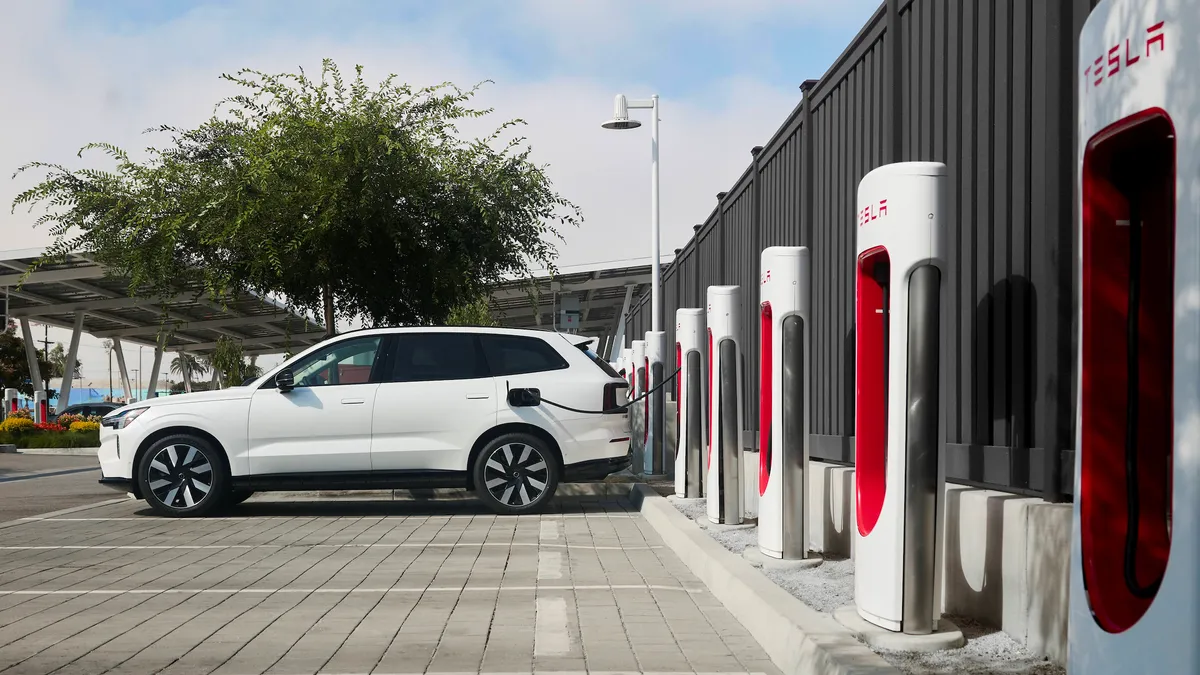 A white Volvo EX90 electric SUIV plugged in for charging at a Tesla Supercharger location.